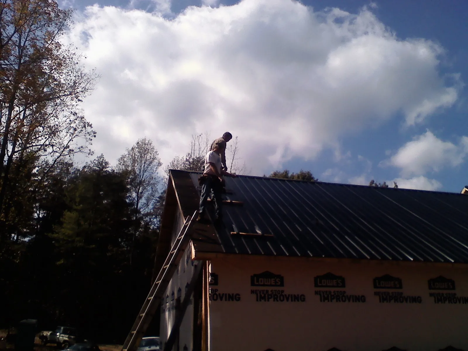 Roofer fastening dark metal panels high against a cloudy sky, from a Roof Inspection job in Westport